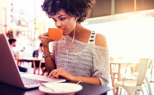 Woman in café sips a drink while reading  on her laptop.